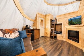 Ein Zeltinneres mit einer Couch, einer kleinen Küchenzeile, einem Kamin und einem Fernseher.