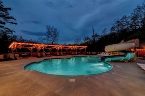 Una piscina con tobogán, rodeada de sillones de descanso y una zona de estar cubierta con luces colgantes.
