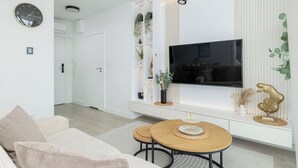 Ett modernt vardagsrum med en platt-TV, en soffa, ett matbord och inbyggda hyllor med dekorativa föremål.