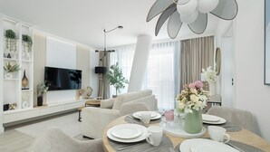 Ett modernt vardagsrum med en platt-TV, en matplats med ett bord för två personer och en soffa.