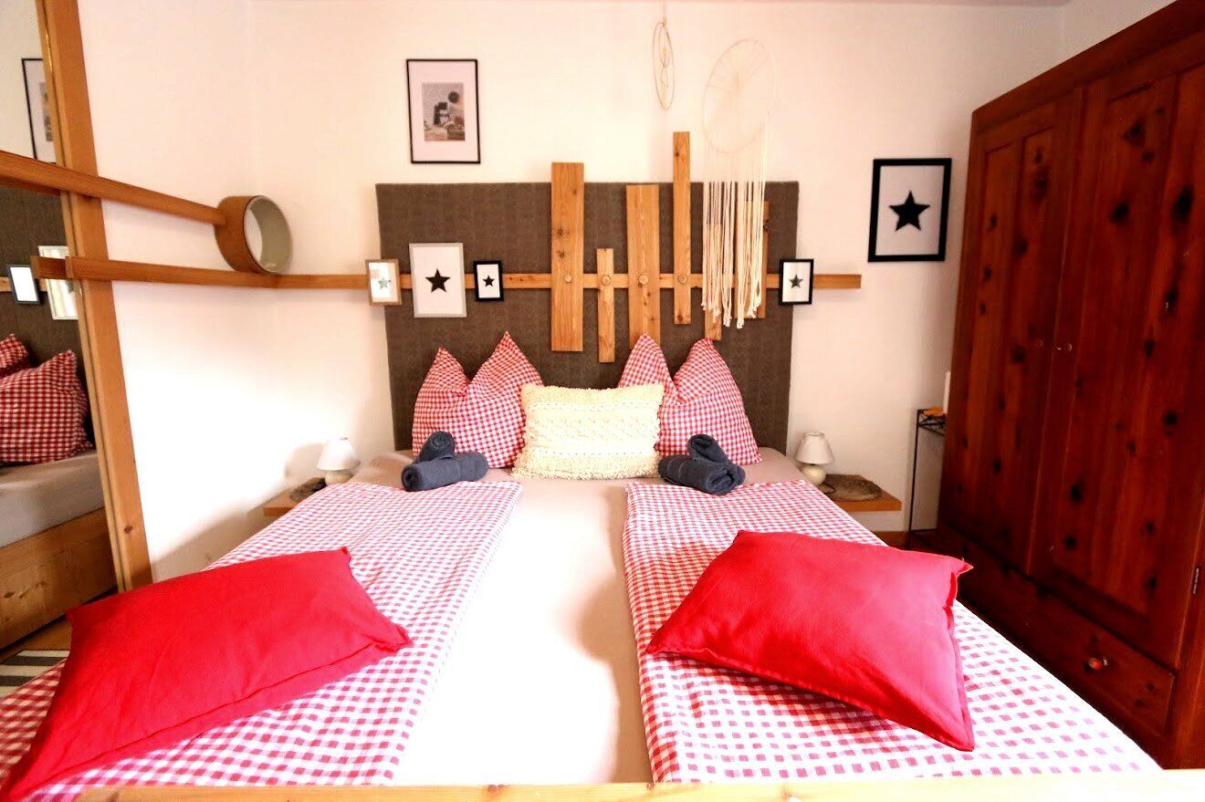 A double bed with checkered bedding, a wooden headboard with a dreamcatcher, and a mirror on the wall.