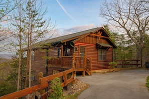 A log cabin with a porch, a stone foundation, and a clear sky. - SMSkys: Views*Wifi*HotTub*Games*Pets*ResortPool (Sevierville)