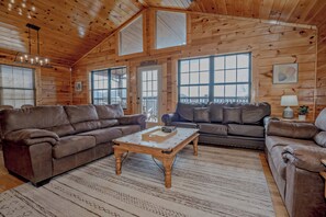 A log cabin interior with two leather sofas, a wooden coffee table, large windows, and a chandelier. - SMSkys: Views*Wifi*HotTub*Games*Pets*ResortPool (Sevierville)