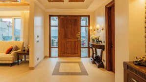 A spacious hallway with a wooden door, a sofa, a console table with decorative items, and a view through the door. - ELIVAAS privé Royce Rose 4BHK Hilltop (Kasauli)