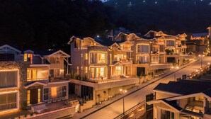 A row of modern, multi-story houses with balconies and large windows, illuminated at night. - ELIVAAS privé Royce Rose 4BHK Hilltop (Kasauli)