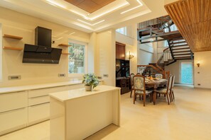 A modern kitchen with a central island, wooden staircase, and a dining area with chairs and a table. - ELIVAAS privé Royce Rose 4BHK Hilltop (Kasauli)