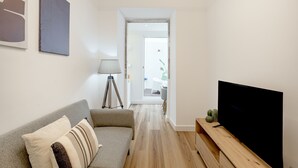 A living room with a sofa, a lamp, a flat-screen TV, and a hallway leading to a door. - GRA A Terrace by Homing (Lisbon)