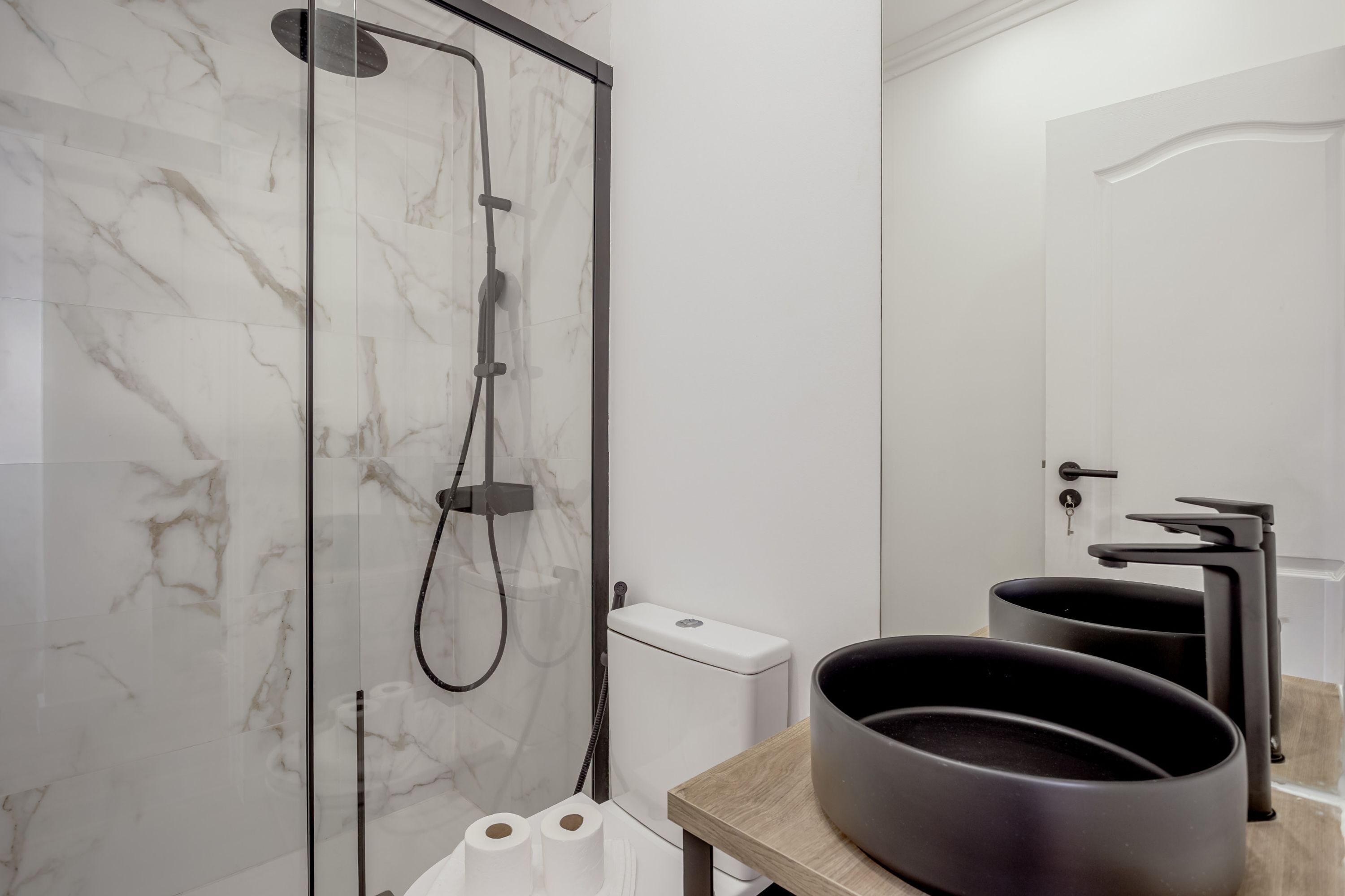 A modern bathroom with a glass-enclosed shower, a toilet, and a sink with a black basin.