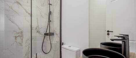 A modern bathroom with a glass-enclosed shower, a toilet, and a sink with a black basin.