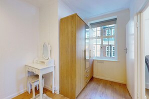 Ein Zimmer mit weißem Schminktisch, Holzschrank und einem Fenster mit Blick auf Gebäude.