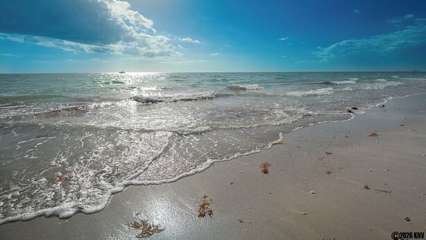 Ein Strand mit Wellen, einem klaren Himmel und einem Boot in der Ferne.