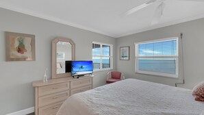Ein Schlafzimmer mit Bett, Kommode, Fernseher und Blick auf das Meer.