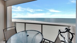 Ein Balkon mit Glastisch und Stühlen, ein Fahrrad und Blick auf Strand und Meer.
