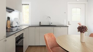 Et moderne køkken med vask, bordplade og skabe. Der er et spisebord med stole og en vase med blomster.