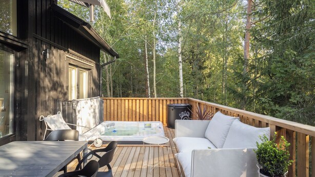 En træterrasse med jacuzzi, udendørs møbler og en skraldespand.