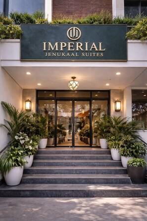 The entrance to Imperial Jenukaal Suites with a modern design, featuring a large sign, steps leading up to the entrance, and potted plants on either side. - Imperial Jenukaal Suites (Kasavanahalli)