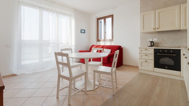 A modern kitchen with white cabinets, a red sofa, and a dining table with chairs. - Cozy 50m2 apartment, perfect for 4 people, located on the 5th floor of a building with lift just 500m from Parco Nord, the largest green area in Milan!At 500m there is the Bruzzano-Parco Nord stop of the S2/S4 suburban train which in just a few stops t (Milan)