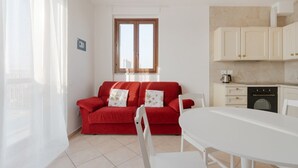 A red sofa with floral cushions, a white dining table, and a kitchen area with cabinets and a coffee machine. - Cozy 50m2 apartment, perfect for 4 people, located on the 5th floor of a building with lift just 500m from Parco Nord, the largest green area in Milan!At 500m there is the Bruzzano-Parco Nord stop of the S2/S4 suburban train which in just a few stops t (Milan)