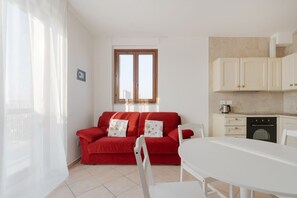 A red sofa with floral cushions, a white dining table, and a kitchen area with cabinets and a coffee machine. - Cozy 50m2 apartment, perfect for 4 people, located on the 5th floor of a building with lift just 500m from Parco Nord, the largest green area in Milan!At 500m there is the Bruzzano-Parco Nord stop of the S2/S4 suburban train which in just a few stops t (Milan)