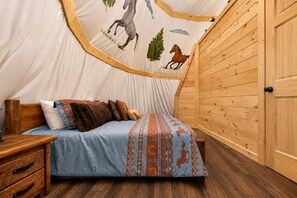 Ein Zeltraum mit Bett, Holzwänden und einer Tür.