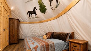 Ein Zelt mit Bett, Holzmöbeln und einer Wand mit Bildern von Pferden und Bäumen.