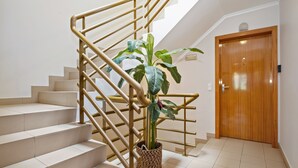 Een trap met beige treden, een gouden leuning, een potplant en een houten deur.