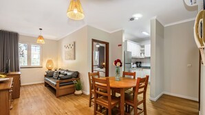 Een moderne woonkamer met een houten eettafel, een bank en een keuken op de achtergrond.