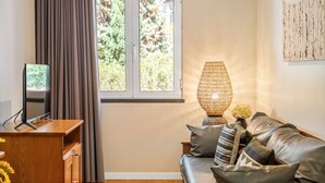 Een kamer met een houten bureau, een televisie, een raam met gordijnen, een bank met kussens en een wandlamp.