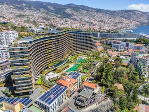 A modern hotel with a curved facade, multiple balconies, a rooftop pool, and solar panels. - Imperatriz 3F by Homie (Funchal)