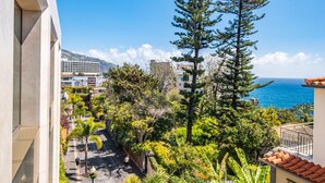A balcony with a view of a coastal area, including a tall pine tree and a building with a tiled roof. - Imperatriz 3F by Homie (Funchal)