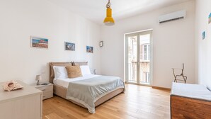 Een slaapkamer met een bed, nachtkastje, lamp en uitzicht door een raam.