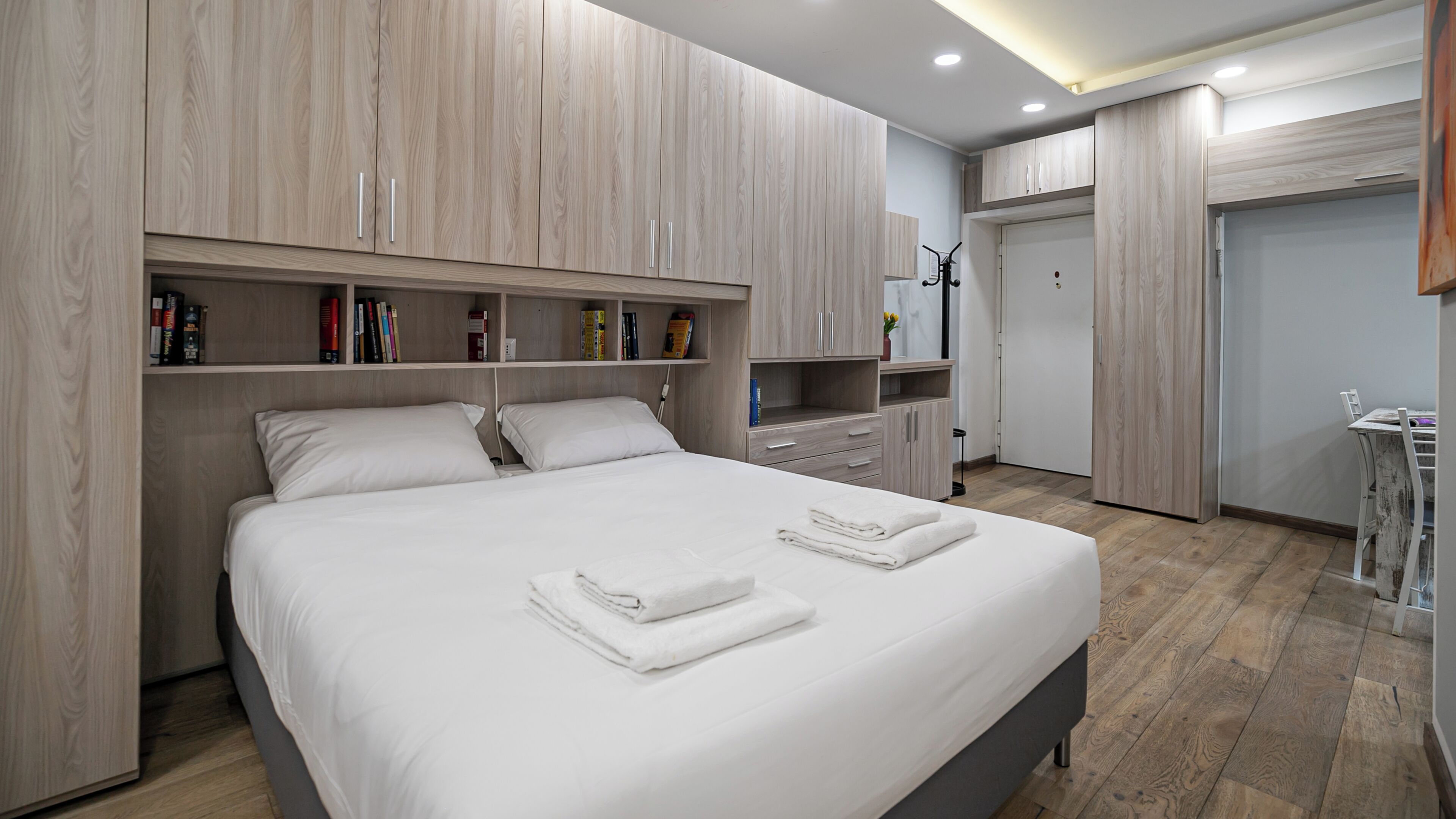 Camera da letto moderna con un letto grande, scaffali a muro, un armadio e un piccolo angolo studio.