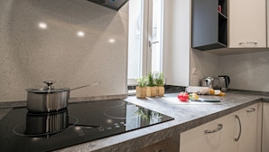 A modern kitchen with a built-in induction cooktop, a pot, a cutting board, fresh vegetables, and a coffee maker. - Italianway Easy - Buenos Aires 2 A (Milan)