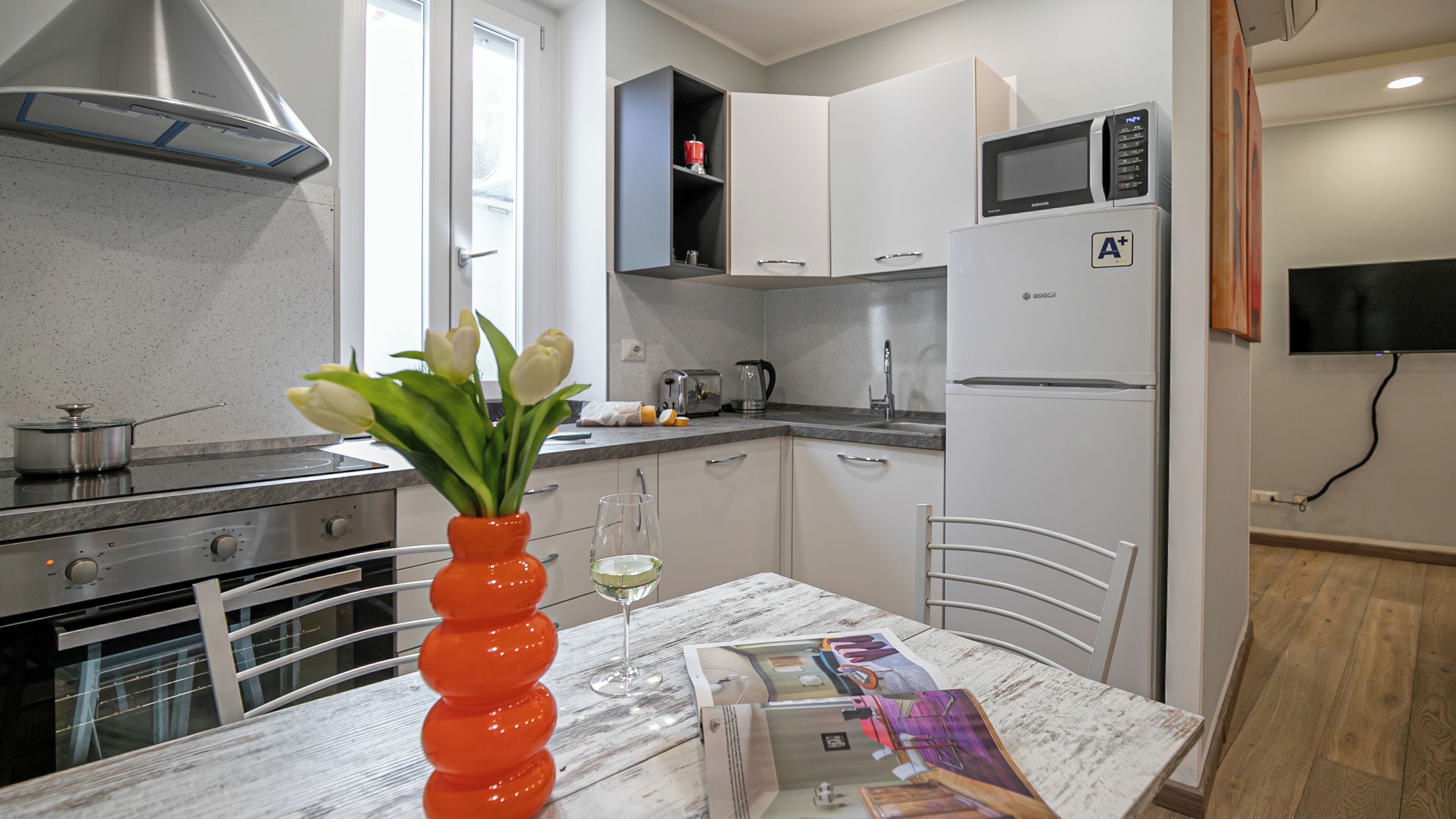 A modern kitchen with white cabinets, a Bosch refrigerator, a microwave, and a sink.