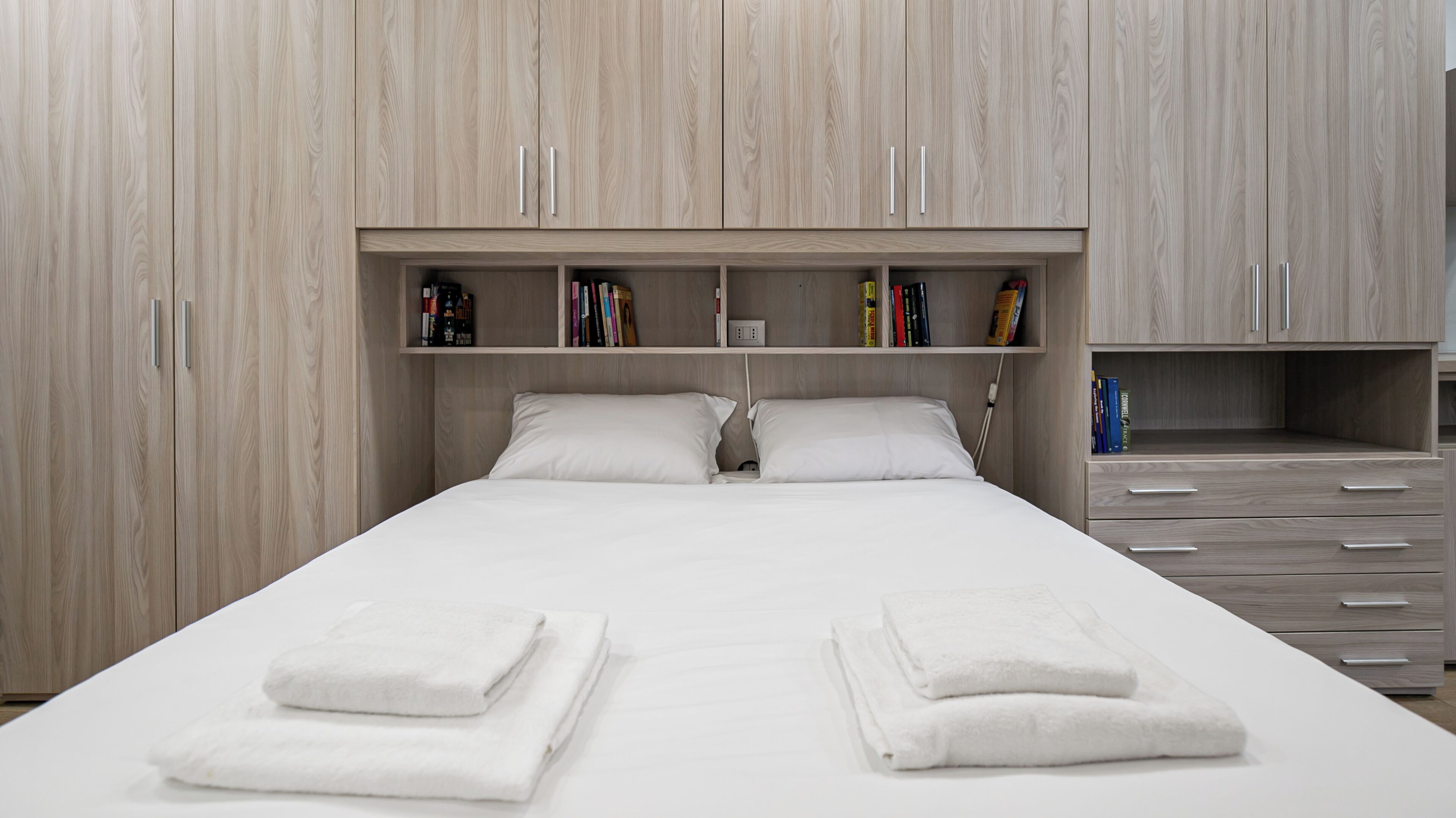 Een moderne hotelkamer met een groot bed, twee nachtkastjes, een inbouwboekenkast en een inloopkast met schuifdeuren.