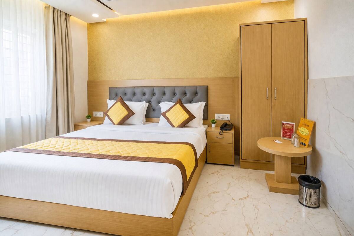 A hotel room with a bed, bedside table, nightstand, wardrobe, and a small round table with a trash bin.