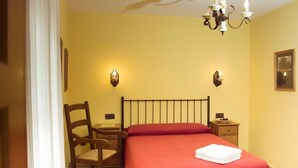 A room with a bed, a chair, a bedside table, a nightstand, and a wall-mounted lamp.