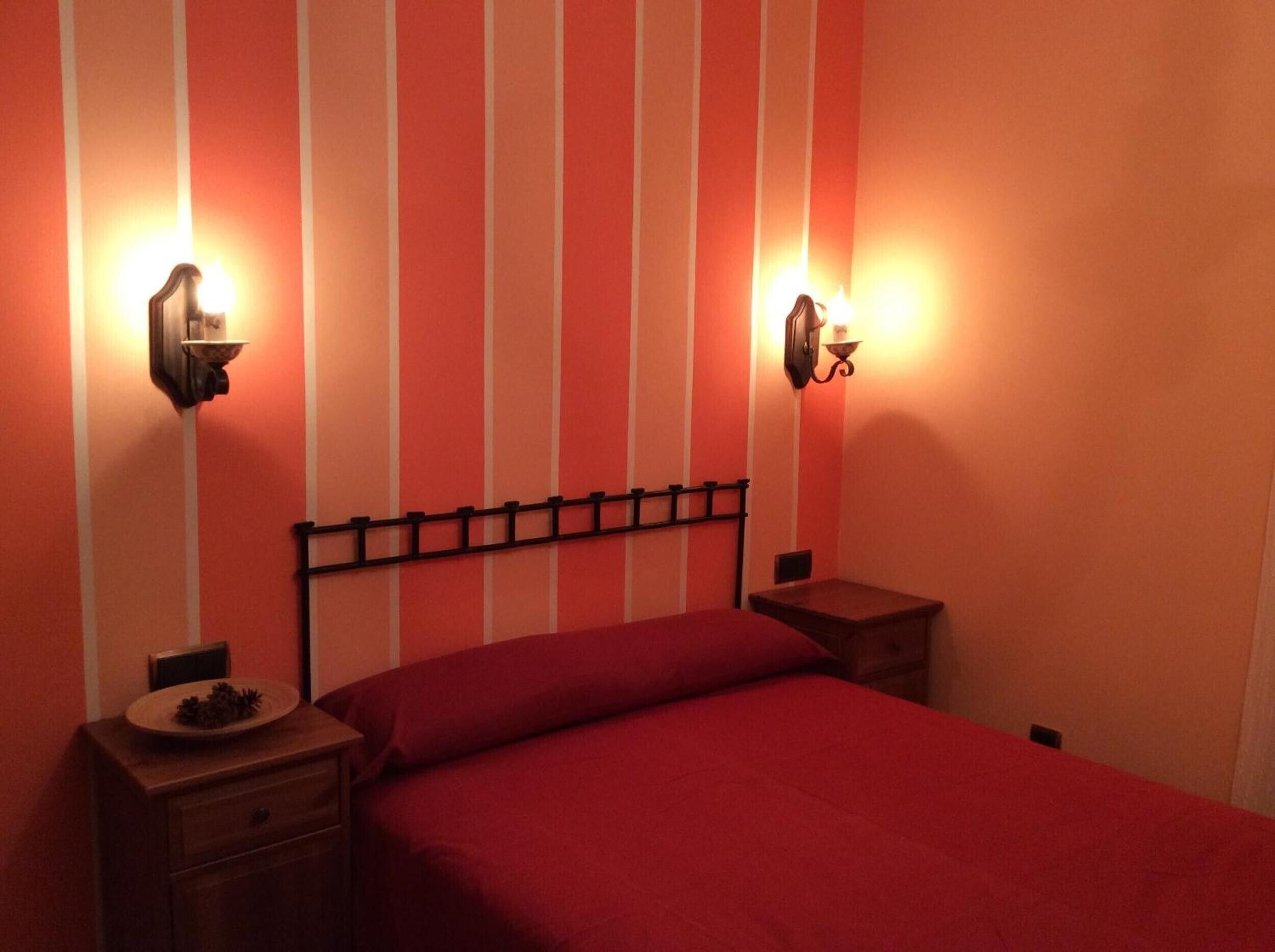 Una cama con cabecera, dos mesitas de noche y lámparas fijadas a la pared.