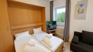 Habitación de hotel con dos camas, televisión, sofá y ventana con vista a áreas verdes.
