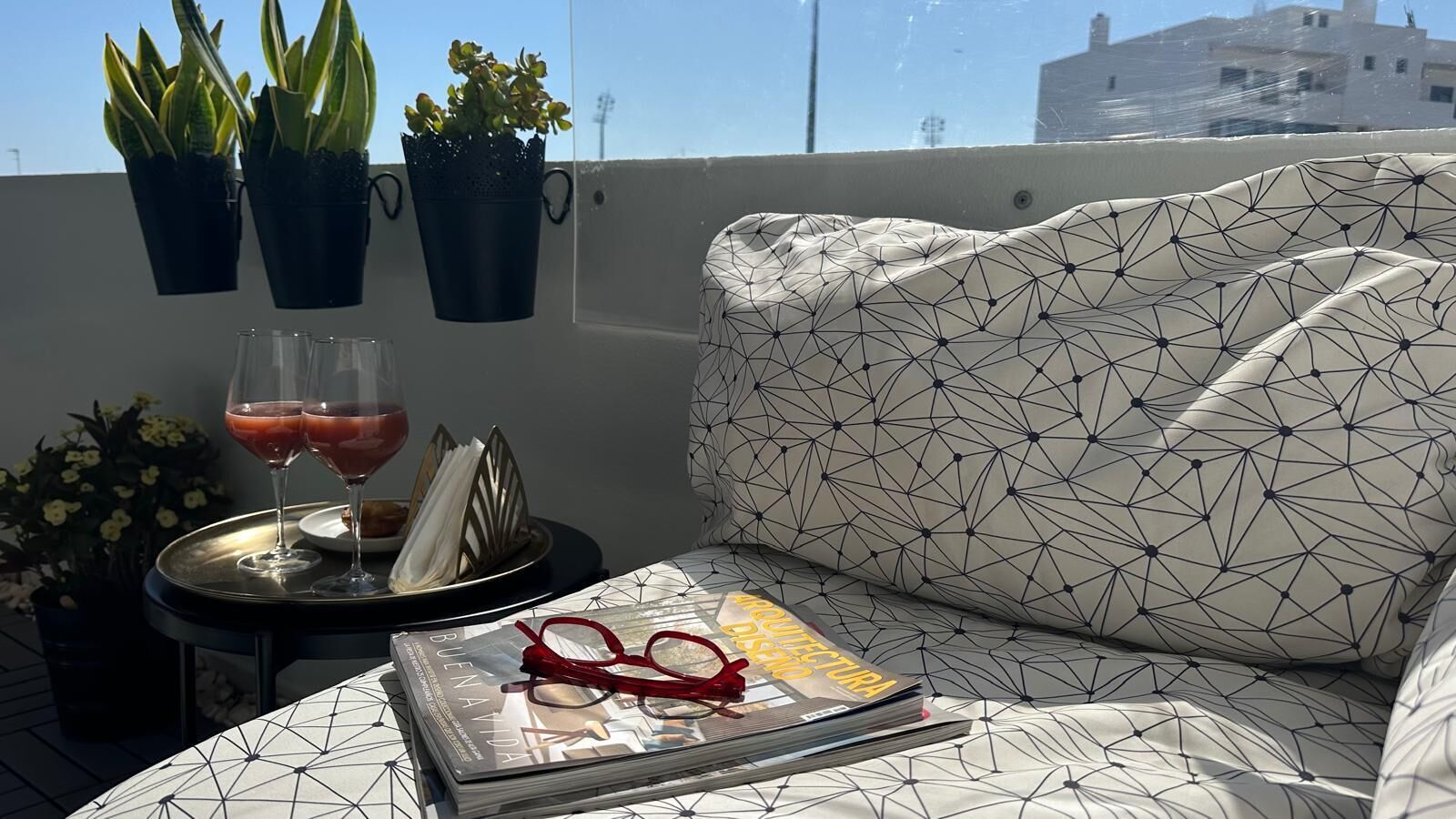Een balkon met een bank, een klein tafeltje met drankjes en glazen, en potplanten.
