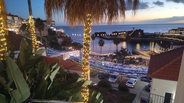 Un balcon donnant sur une rue décorée et sur la mer au crépuscule.