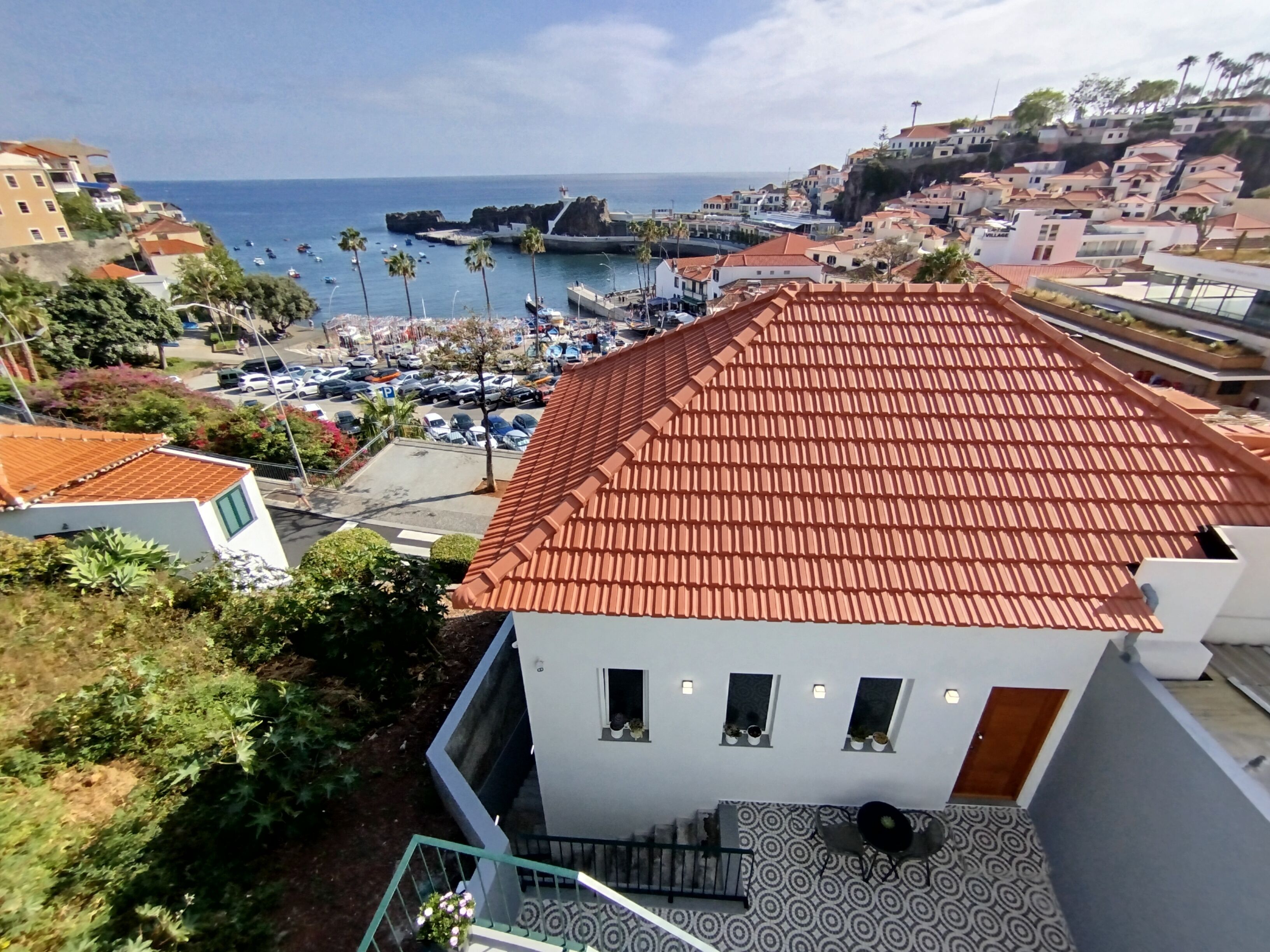 A coastal town with terracotta-roofed buildings, a marina with boats, and a clear view of the sea.