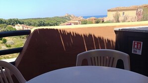 Eine Terrasse mit Tisch und Stühlen mit Blick auf eine Küstenlandschaft mit Gebäuden und Grünflächen.