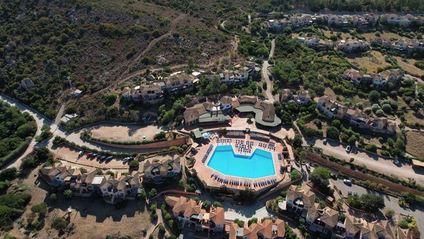 Ein Luftbild zeigt ein Resort mit einem zentralen Schwimmbecken, mehreren Gebäuden und umliegender Bepflanzung.
