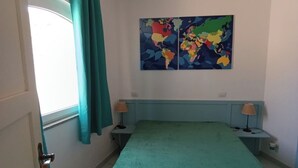 Ein Schlafzimmer mit einem Bett, zwei Nachttischen, einem Deckenventilator, einem Fenster mit Vorhängen und einer Weltkarte als Wandbild.