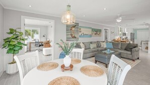 Een moderne woonkamer met een witte eettafel, een grijze bank en een hanglamp.