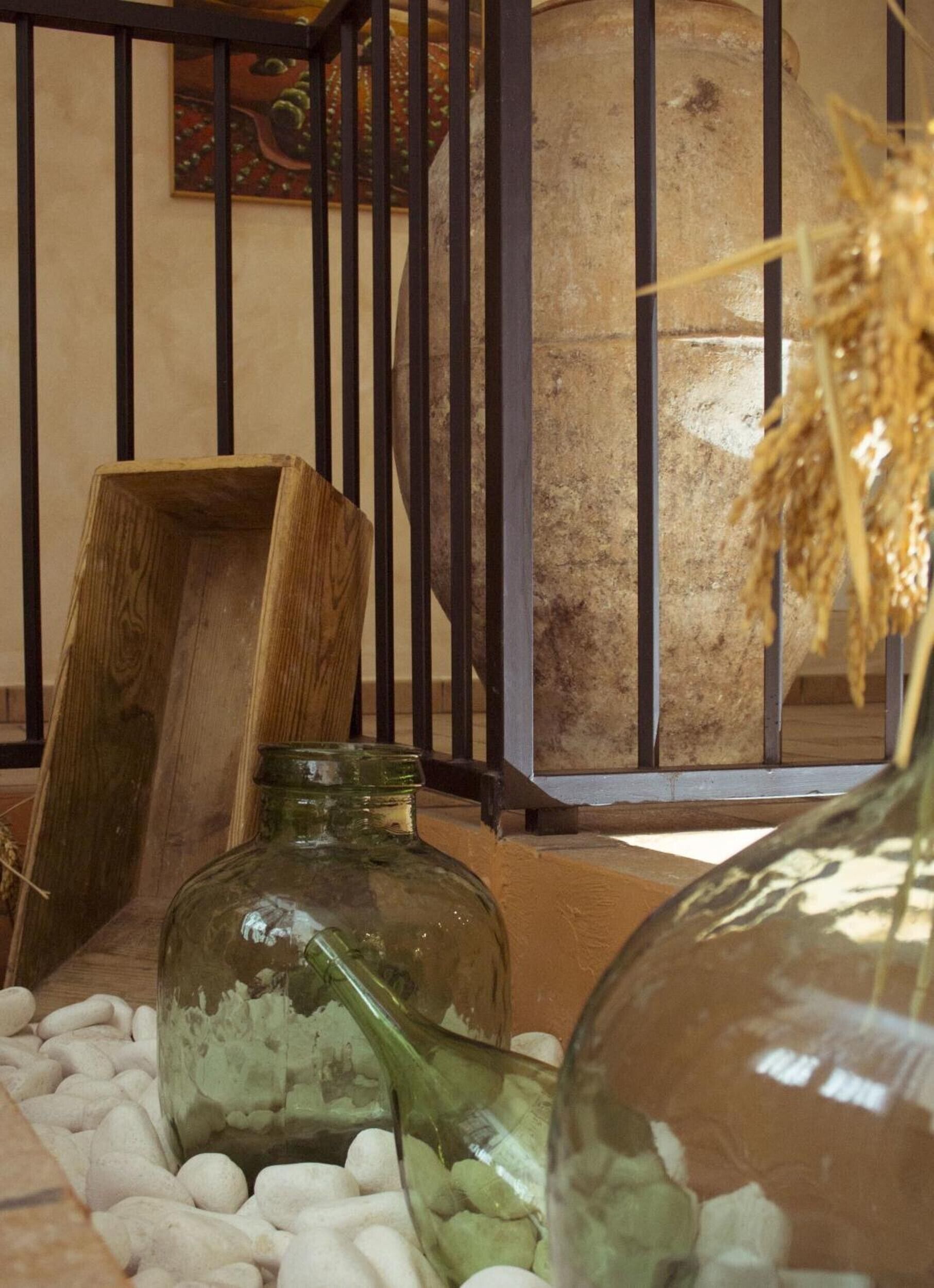 Ein rustikales Interieur mit einem Holzstuhl, einer grünen Glasflasche und einem Metallkäfig.