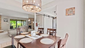 A dining area with a wooden table, woven placemats, and a chandelier. - Lake Ozark Oasis Central Location & Pool Access (Lake Ozark)