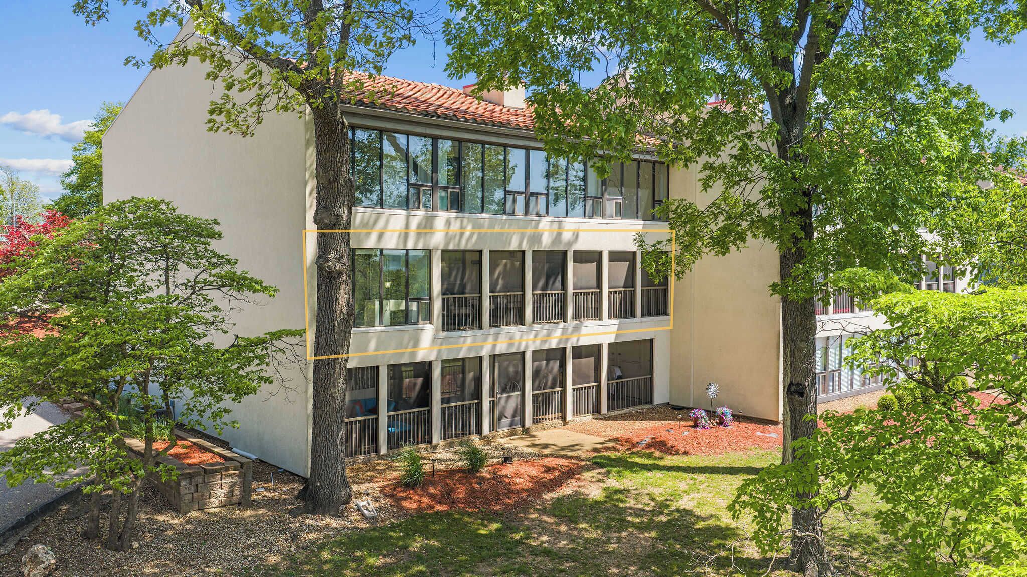A modern building with a flat roof, large windows, and a courtyard with trees and a small garden area.