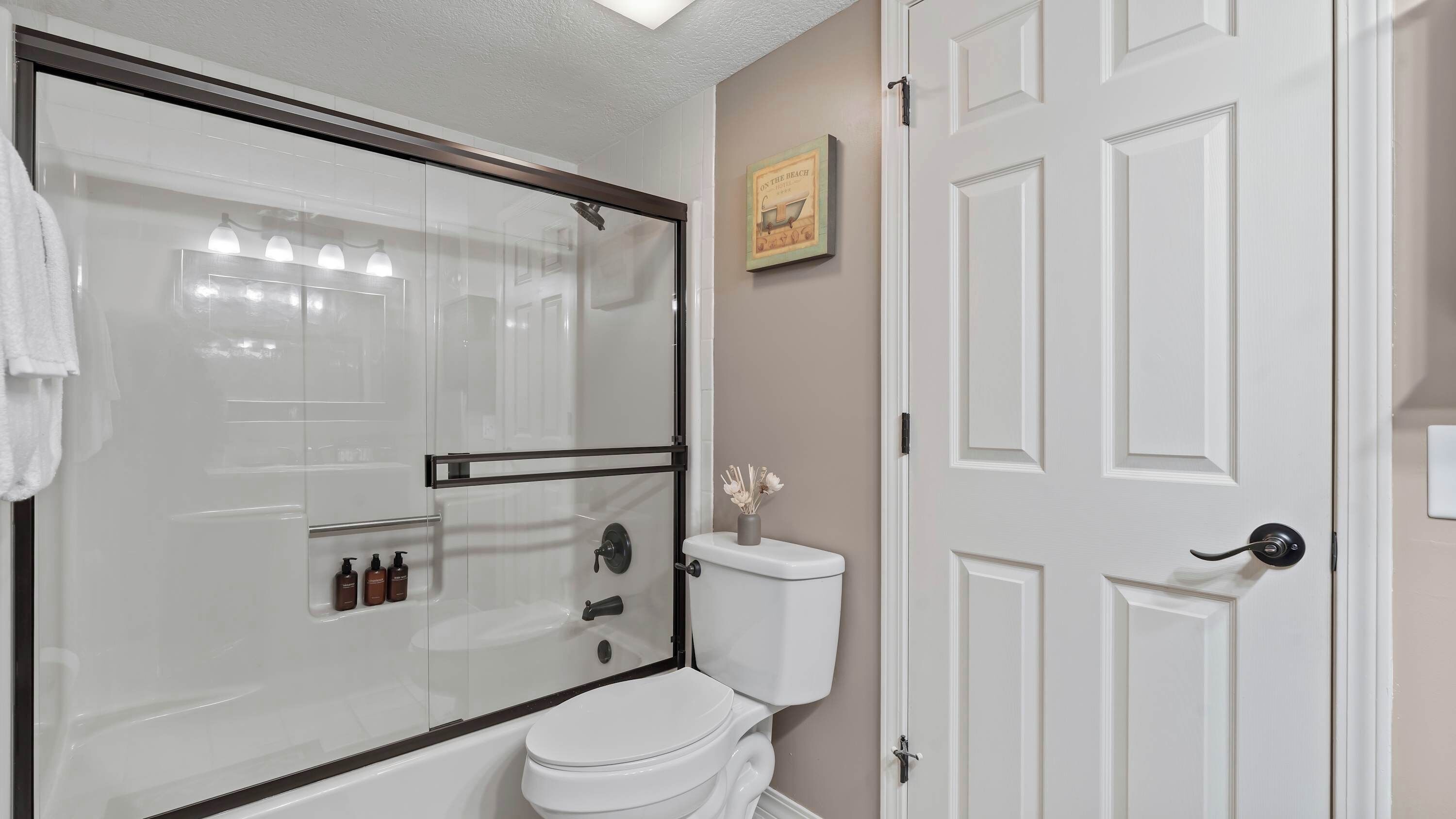 A bathroom with a glass-enclosed shower, a toilet, and a white door.